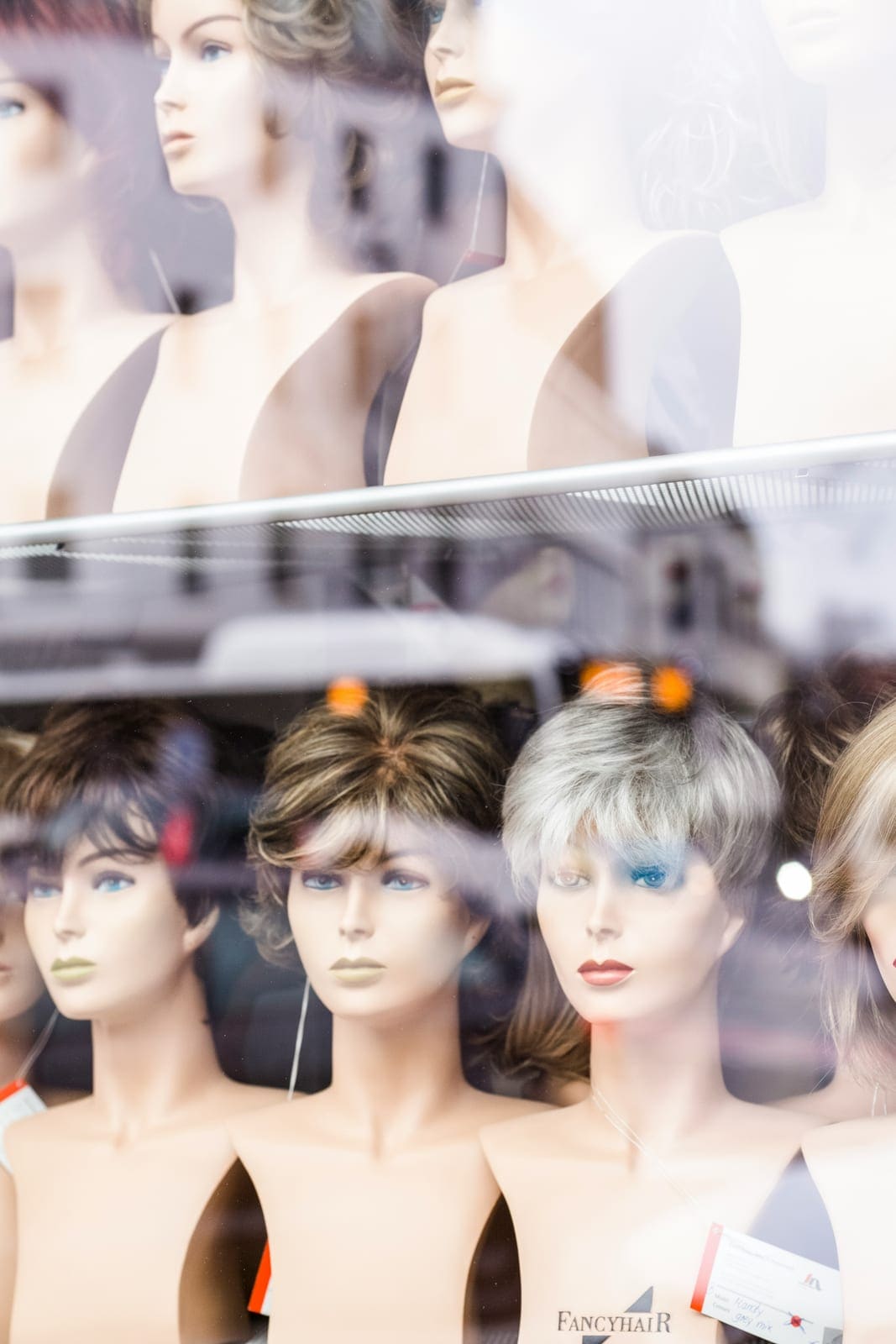 Perücken in verschiedenen Farben und Längen auf Modellköpfen im Schaufenster
